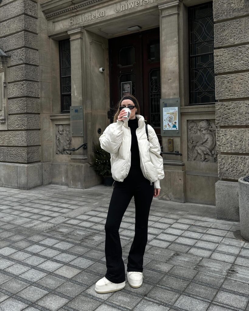 Woman outside a European university library in a cream cropped puffer jacket, black turtleneck, black flared trousers and white moon boots