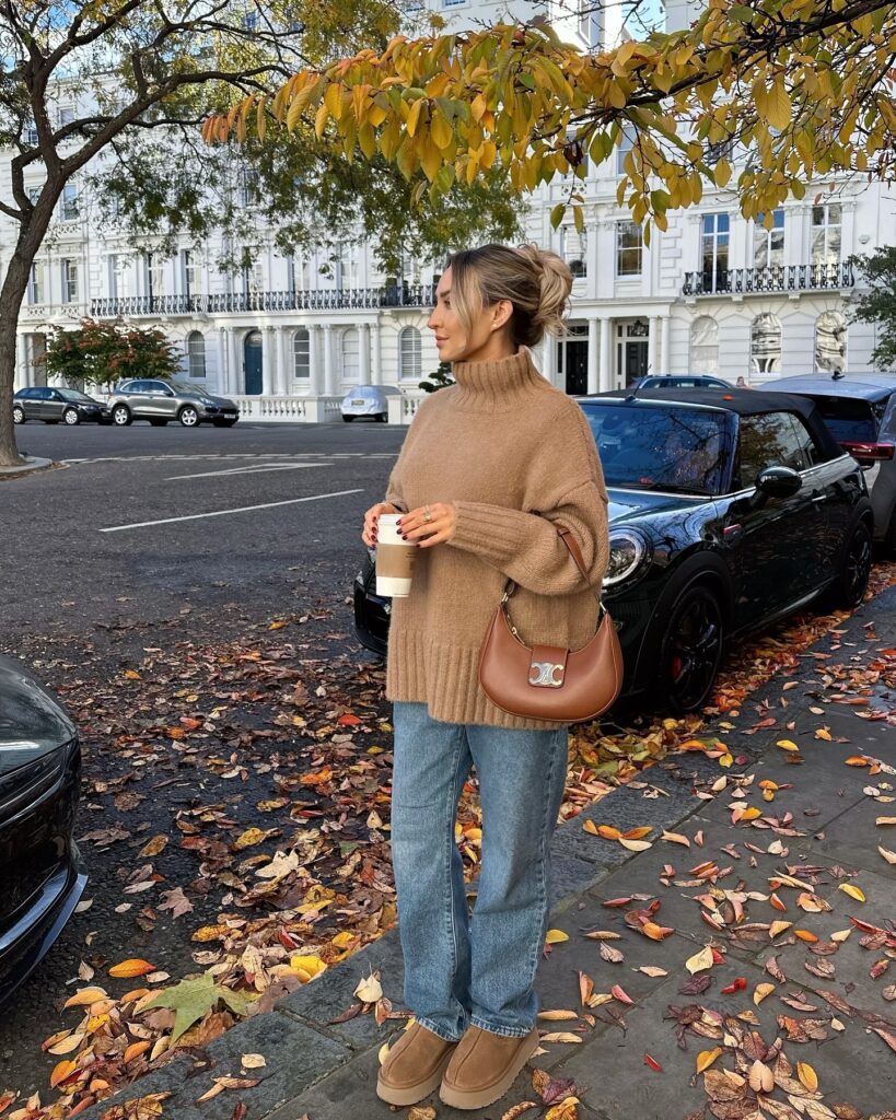 Woman on a leafy London street in an oversized camel turtleneck jumper with straight-leg jeans, tan platform Ugg boots and a brown shoulder bag