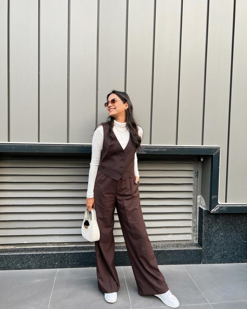 Petite woman in a matching brown pinstripe waistcoat and wide-leg trousers over a white turtleneck with white sneakers
